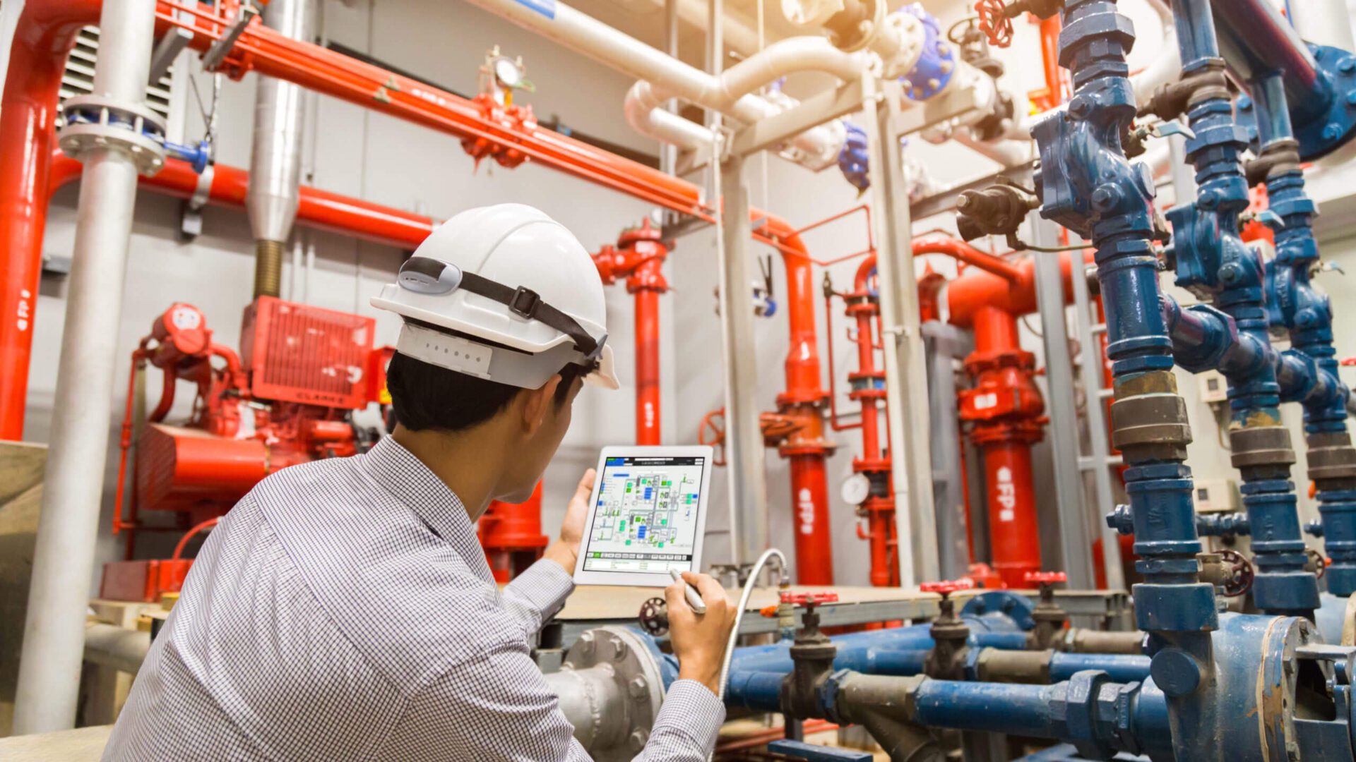 A man in white shirt holding laptop near pipes.